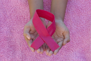 person holding a pink ribbon in her hands over a pink blanket background